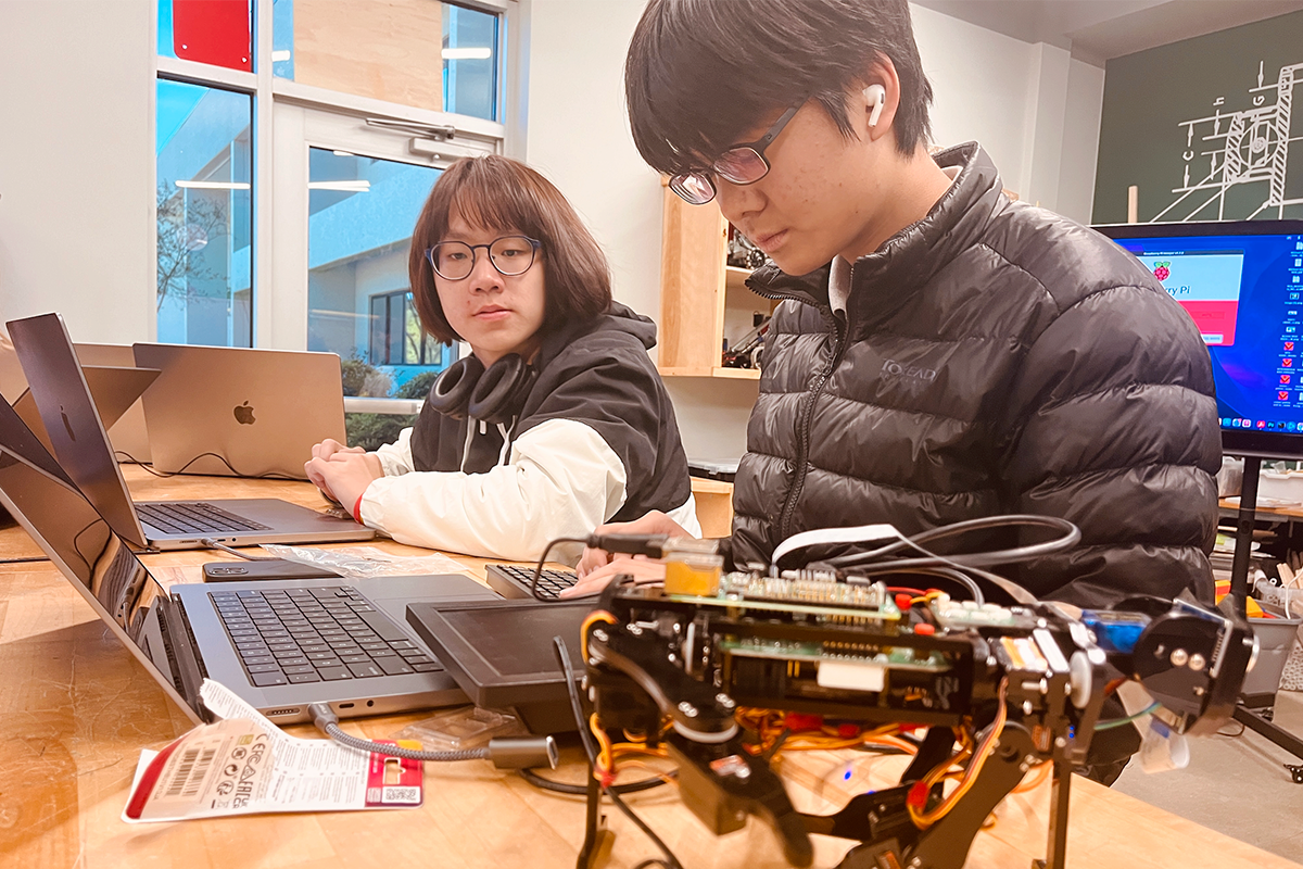 Students programming robot with laptops